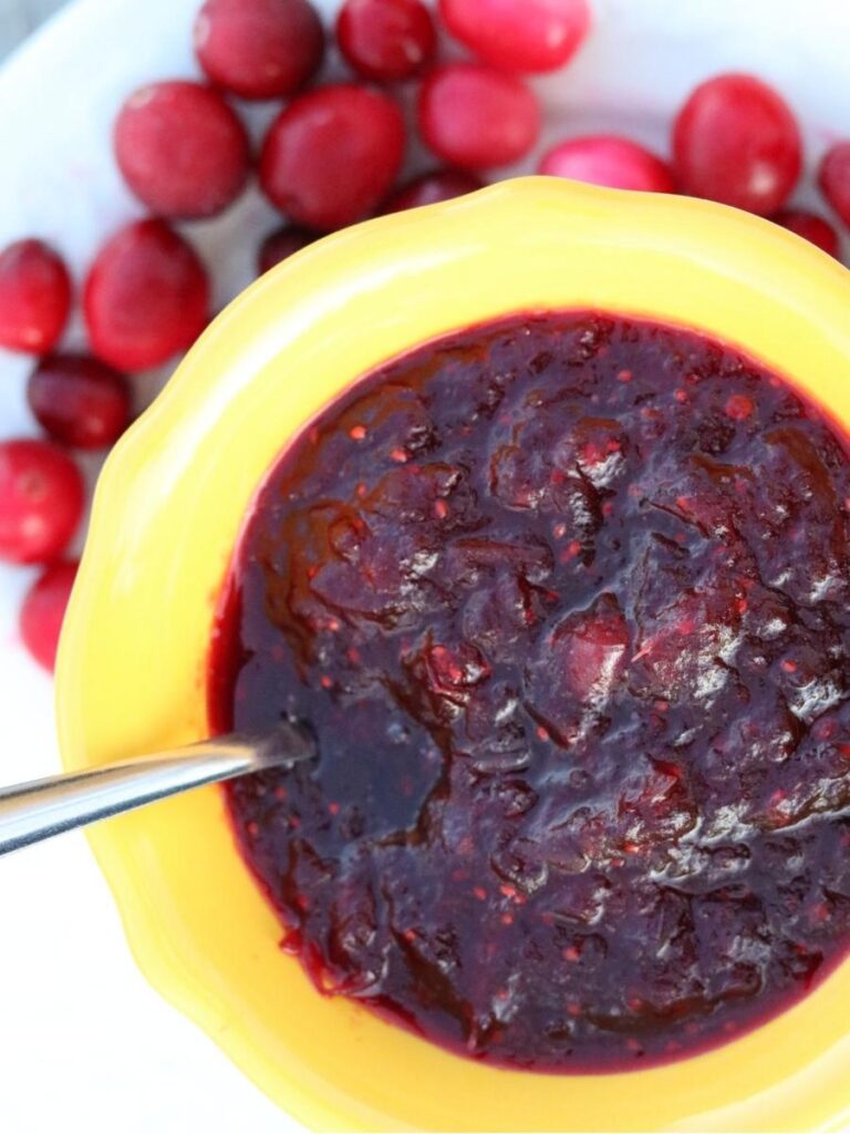 small yellow bowl of homemade cranberry sauce on a plate with fresh cranberries