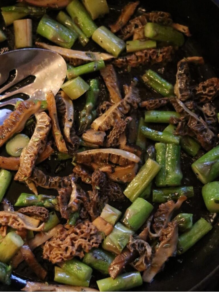 sautéed morels and asparagus in a cast iron pan with a metal spoon